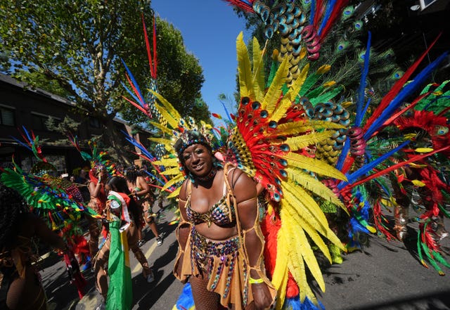 A dancer with a multicoloured costume of feathers forming 'wings' at the Notting Hill Carnival with other dancers in the background