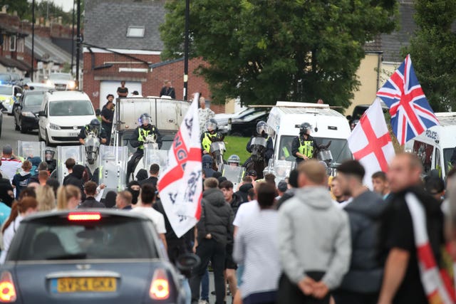 Protesters waving England flags confront riot police, some mounted on horses, on a street in Sunderland