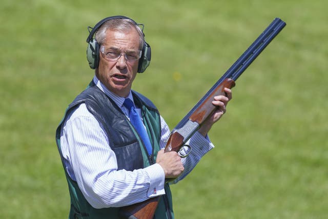 Nigel Farage holding a shotgun while wearing ear defenders against a bright grassy backdrop