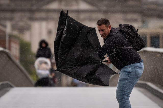 A man struggling with his umbrella on Millennium Bridge in London 