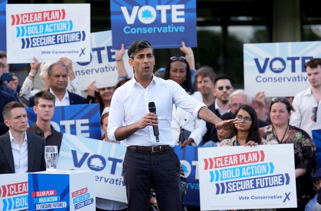Rishi Sunak in shirt sleeves holding a microphone and backed supporters holding 'Vote Conservative' placards