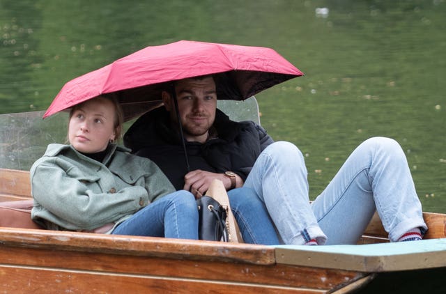 People shelter under umbrellas whilst punting along the River Cam in Cambridge