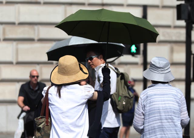 Tourists shelter from the sun under umbrellas in London