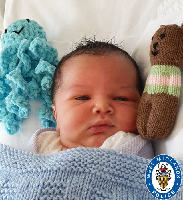 Baby boy laying in cot with soft knitted toys either side of his head