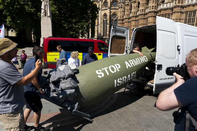 a pretend weapon with 'stop arming Israel' written on its side being loaded into a van by protesters