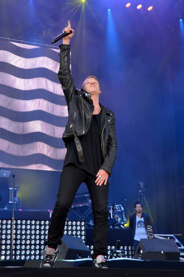 Macklemore performing on stage, with one hand raised pointing into the air