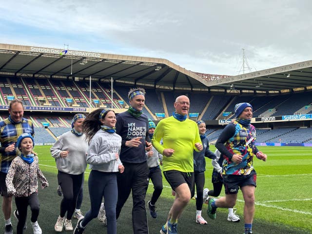 John Swinney jogging with others around the edge of the pitch at Murrayfield stadium