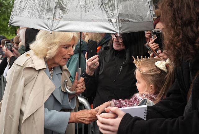 Camilla shakes hands with a young girl who is wearing a tiara