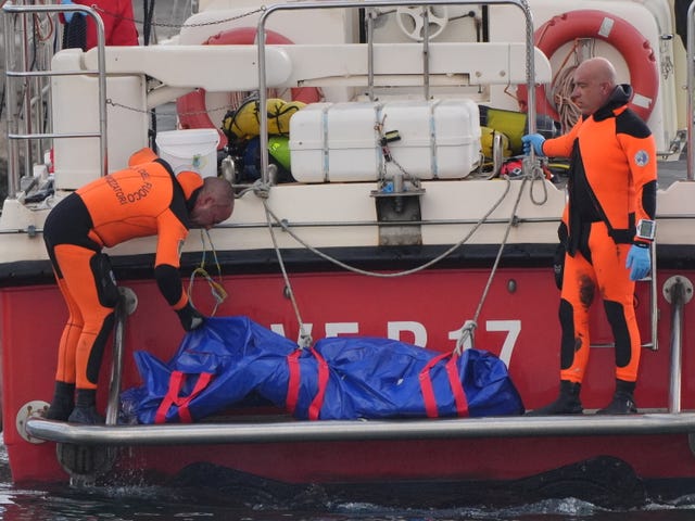 The fifth body bag is brought ashore at the harbour in Porticello by rescue workers searching for tourists missing after the luxury yacht Bayesian sank in a storm