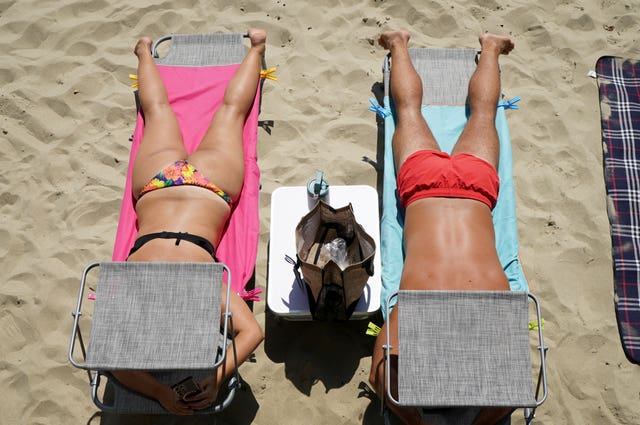 Two people lying on a beach with their heads covered 
