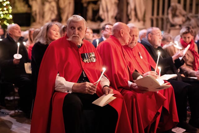 Chelsea Pensioners wearing red cloaks and holding candles