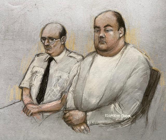 A court sketch of Gavin Plumb dressed in white sitting beside a custody officer 