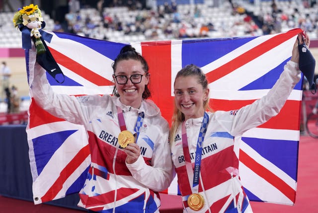 Katie Archibald on the left with Laura Kenny celebrate with their gold medals in Tokyo, with a union flag behind them.