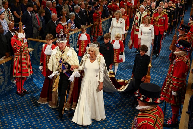 The King and Queen hold hands as they walk side by side in the House of Lords, watched by guests