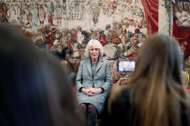 The Queen sitting down with a tapestry backdrop 