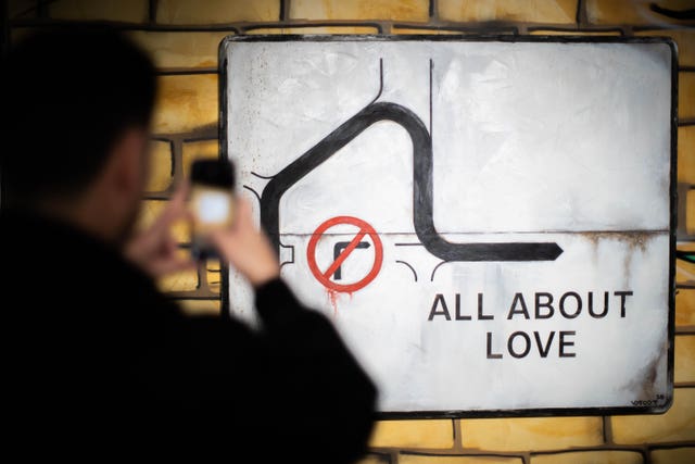 A man takes a photo with a phone of a street sign artwork