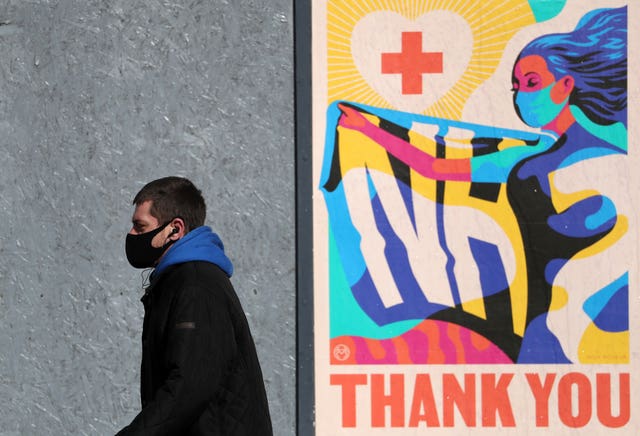 A man in a facemask walks past a poster reading 'NHS Thank-You'