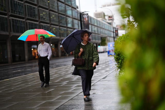 Two people walk along a street in the rain, using umbrellas