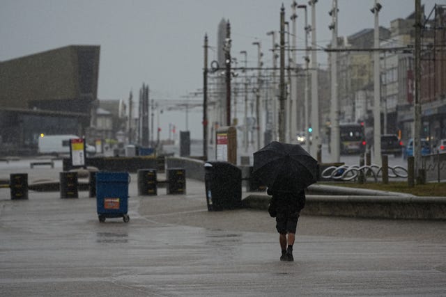 A man takes shelter from the wet weather beneath an umbrella as he walks along the promenade in Blackpool, Lancashire