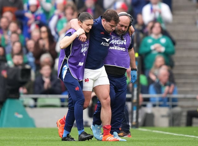 France’s Antoine Dupont leaves the pitch after picking up an injury, with his arms around two medics. 