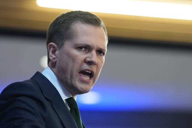 Head and shoulders of a man in a dark suit speaking towards the camera 