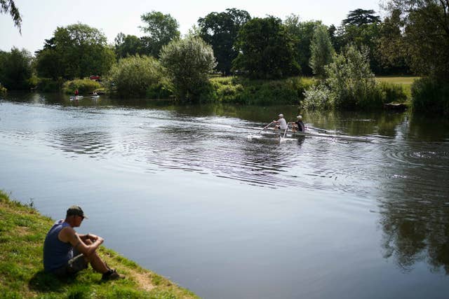 Rowers on a river watched by a man on the riverbank