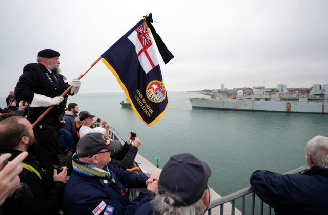 Dick Shenton holding up a naval flag amongst onlookers as HMS Bristol is towed away