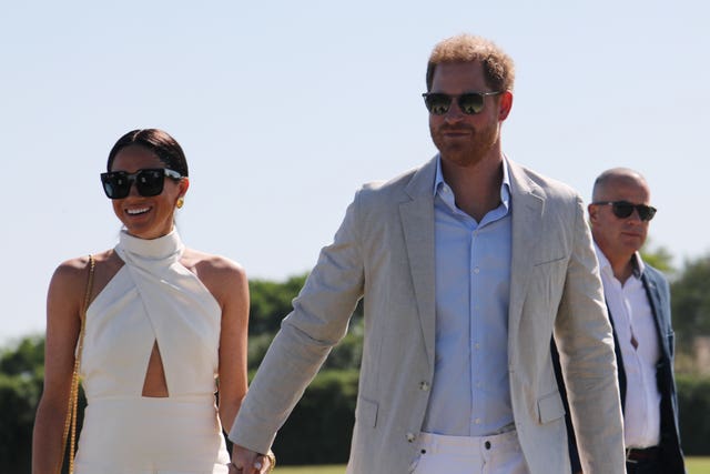 Harry and Meghan wearing sunglasses walking along hand in hand in the sunshine at the polo