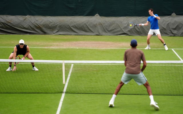Andy Murray hits a forehand from the back of the court while Jamie Murray crouches near the net