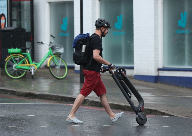 An e-scooter rider pushes his scooter after being stopped by a police officer (Yui Mok/PA)