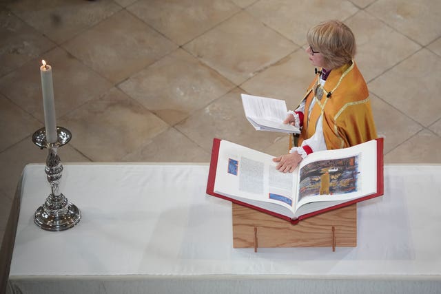 Dame Sarah Mullally holding a sheet of paper, with one hand on a book, at an alter table