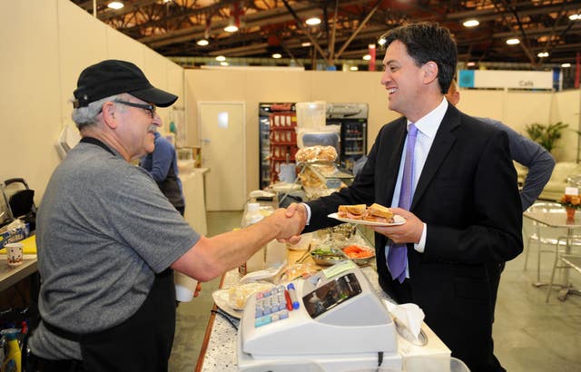 Ed Miliband holding a plate of sandwiches and shaking hands with a shop assistant