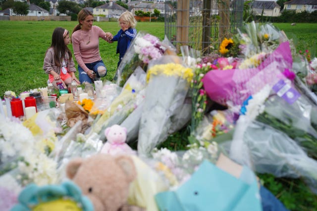 A woman and two young girls look at floral tributes