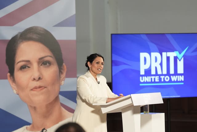 Priti Patel stands at a lectern with blue screen behind her