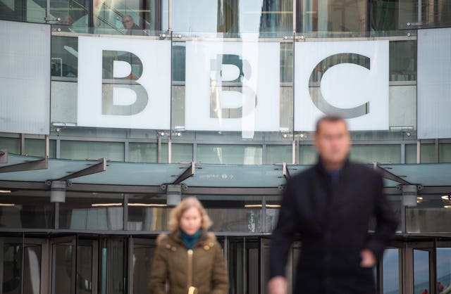 Exterior view of BBC Broadcasting House, with two people in the foreground walking away from the building