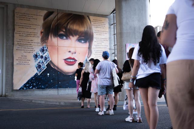 Swifties queue for a photo at a giant mural