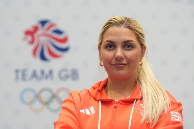 Amber Rutter stands in front of a Team GB logo wearing an orange hoodie. 