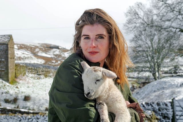 Amanda Owen holding a lamb, with a snowy rural landscape behind her