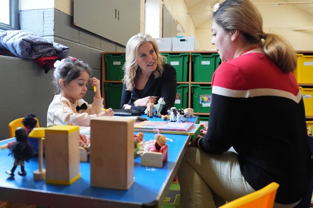 Sophie leans in to a chat to a woman as a young girl plays with toys on a table in Chelmsford