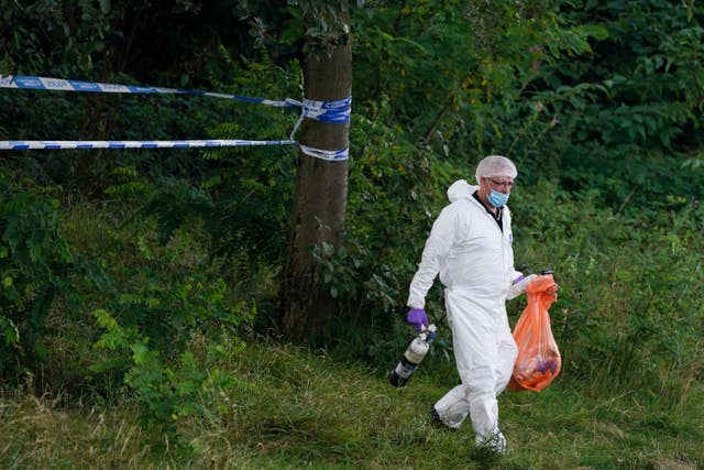 A forensic officer leaves a cordoned-off woodland area