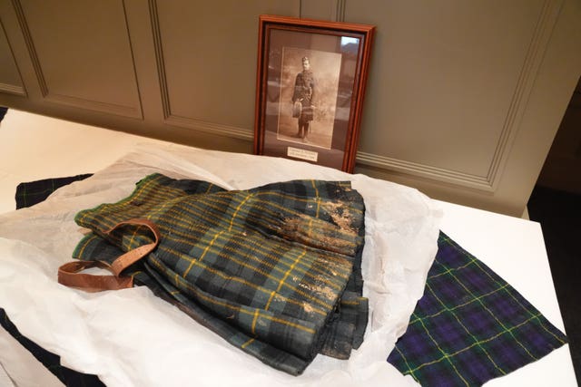 A kilt crusted with mud lies on a museum display table