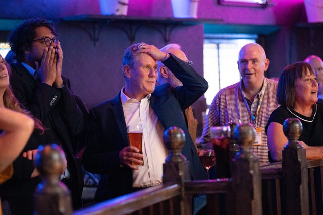 Sir Keir Starmer with a pint in his right hand and his left hand on his head, surrounded by people while watching the Arsenal v Tottenham Hotspur match at The Font pub in Brighton