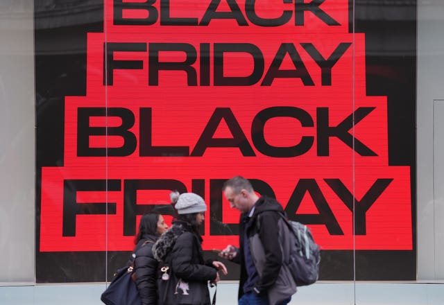 People walk past Black Friday sales signs in a shop window