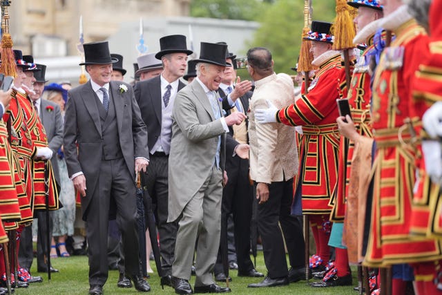 A high-spirited Charles shares a joke with guests at the Buckingham Palace garden party, flanked by the ceremonial Yeomen of the Guard in their distinctive scarlet and gold uniforms