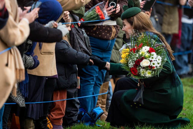 Kate with an arm-full of flowers talks to a child 