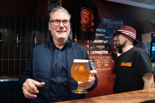 Sir Keir Starmer smiles while holding a drink in a pub