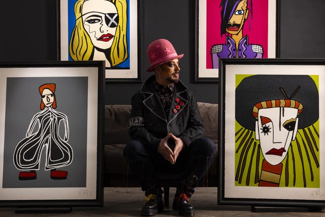 Boy George wearing a pink hat and crouching between four of his portraits