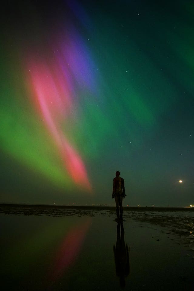 The Northern lights glow on the horizon above sculptures on Crosby Beach, Merseyside