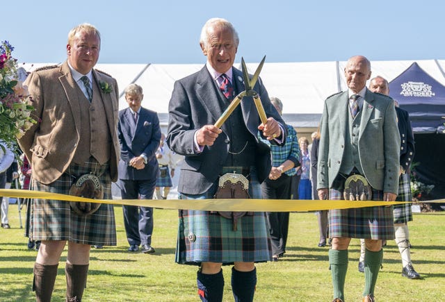 The King, wearing a kilt, uses a pair of gardening shears to cut a ribbon to officially open a flower show