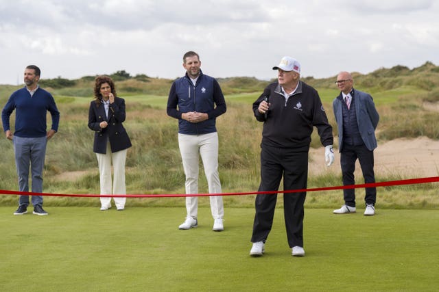 Donald Trump holding a microphone, with his sons Donald Jnr and Eric alongside other dignitaries in the background on a golf course